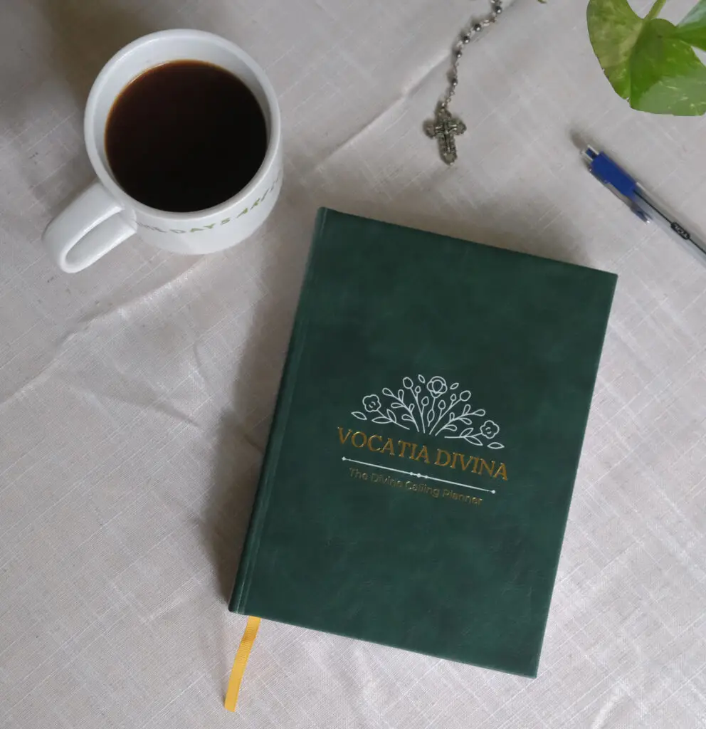 Vocatia Divina planner on table next to coffee, plant and rosary